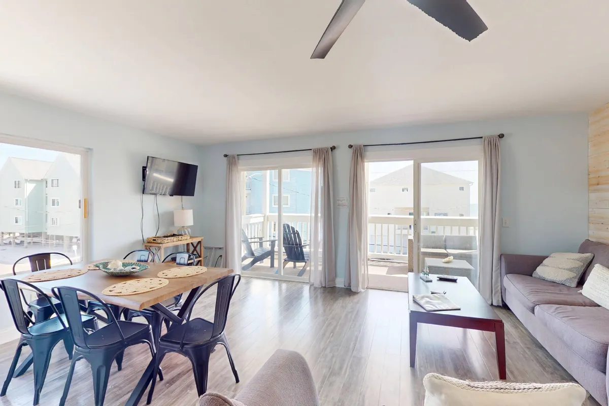 This image features an open, cozy living and dining area with a comfortable sofa, a dining table, and large balcony doors that allow natural light to flood the space. The inviting atmosphere suggests relaxation, group gatherings, and a seamless transition between lounging and dining.