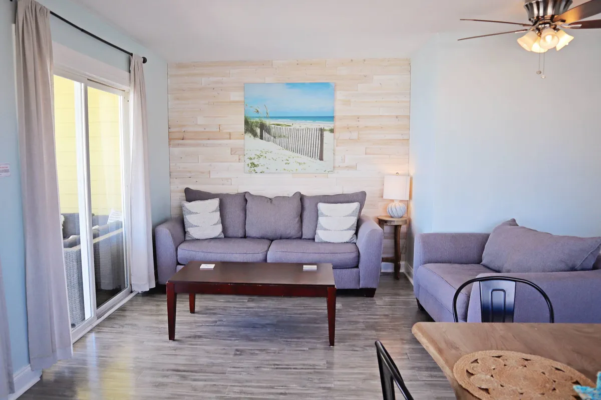 A close-up view of a comfortable sofa, wooden table, and charming wall art, set in a cozy and inviting living area. The scene suggests a perfect spot for relaxing with morning coffee or unwinding after a day at the beach.