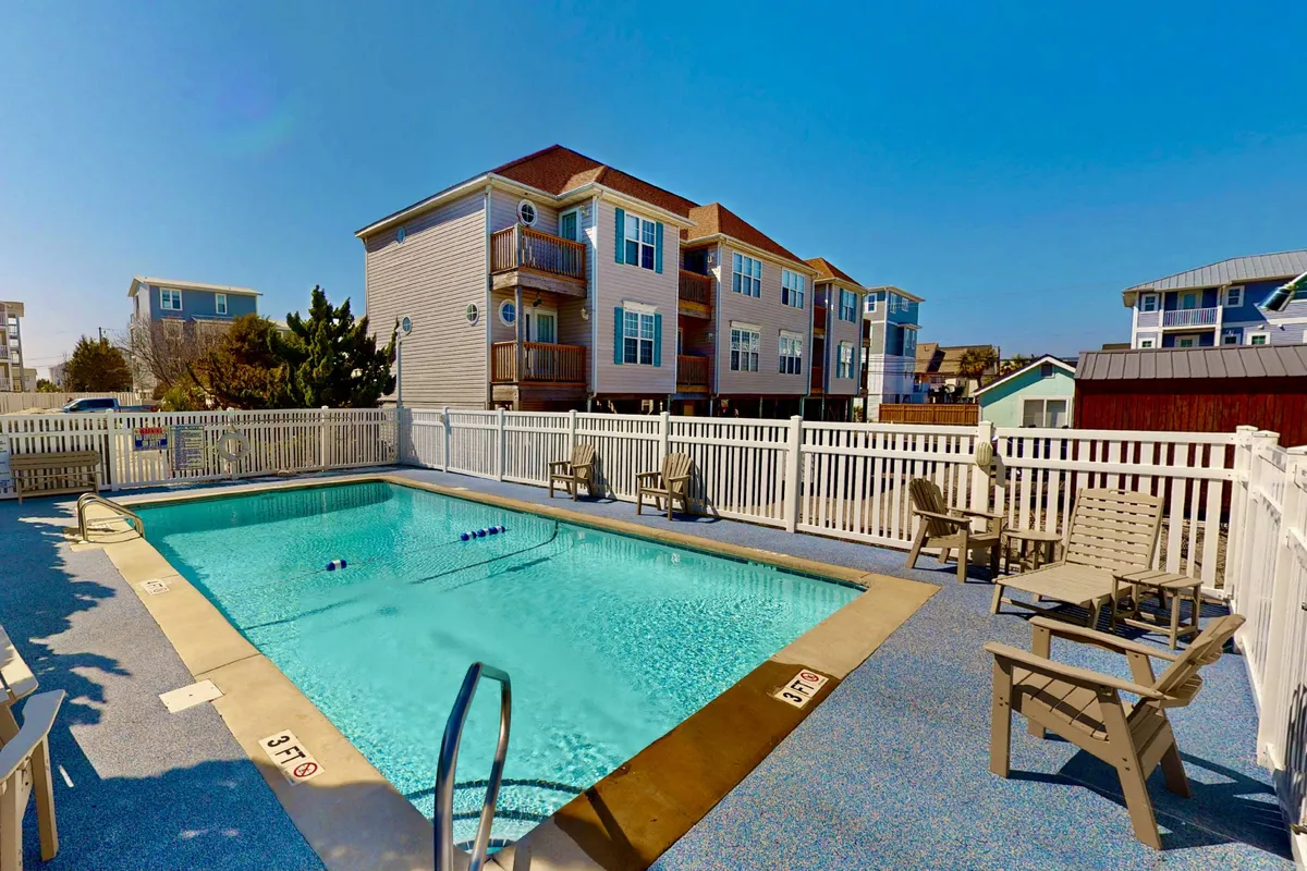 An inviting outdoor pool area surrounded by lounge chairs and framed by nearby buildings. The pool glistens in the sun, evoking a resort-style atmosphere ideal for swimming, sunbathing, and socializing.