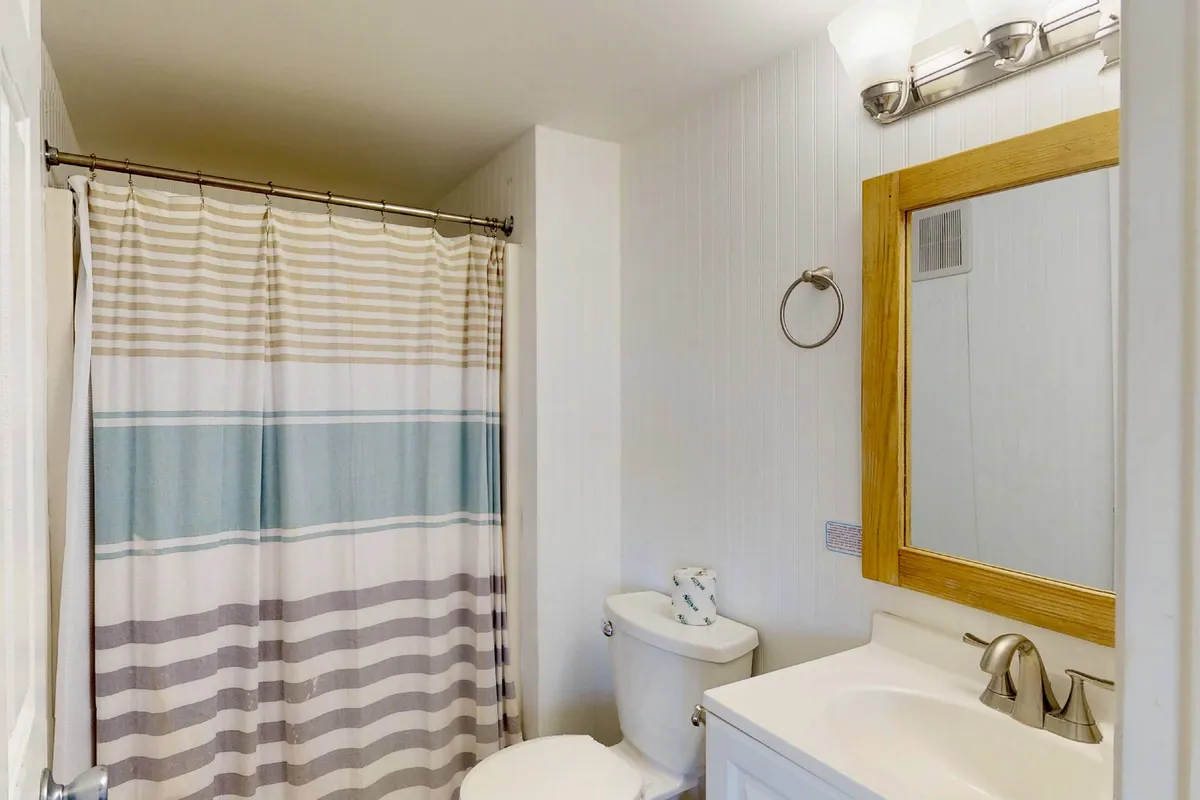 A refreshing bathroom scene with a striped shower curtain, a wooden-framed mirror above a practical sink, and soft lighting that creates a relaxing and clean atmosphere.