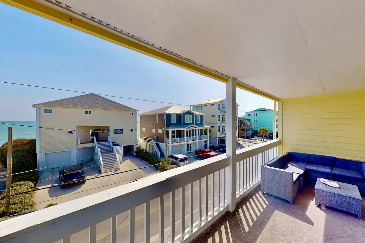 A tranquil balcony seating area with comfortable chairs facing out toward a scenic ocean view, surrounded by neighboring houses. The setting invites relaxation and is perfect for enjoying fresh breezes, sunrise coffee, or starlit cocktails.