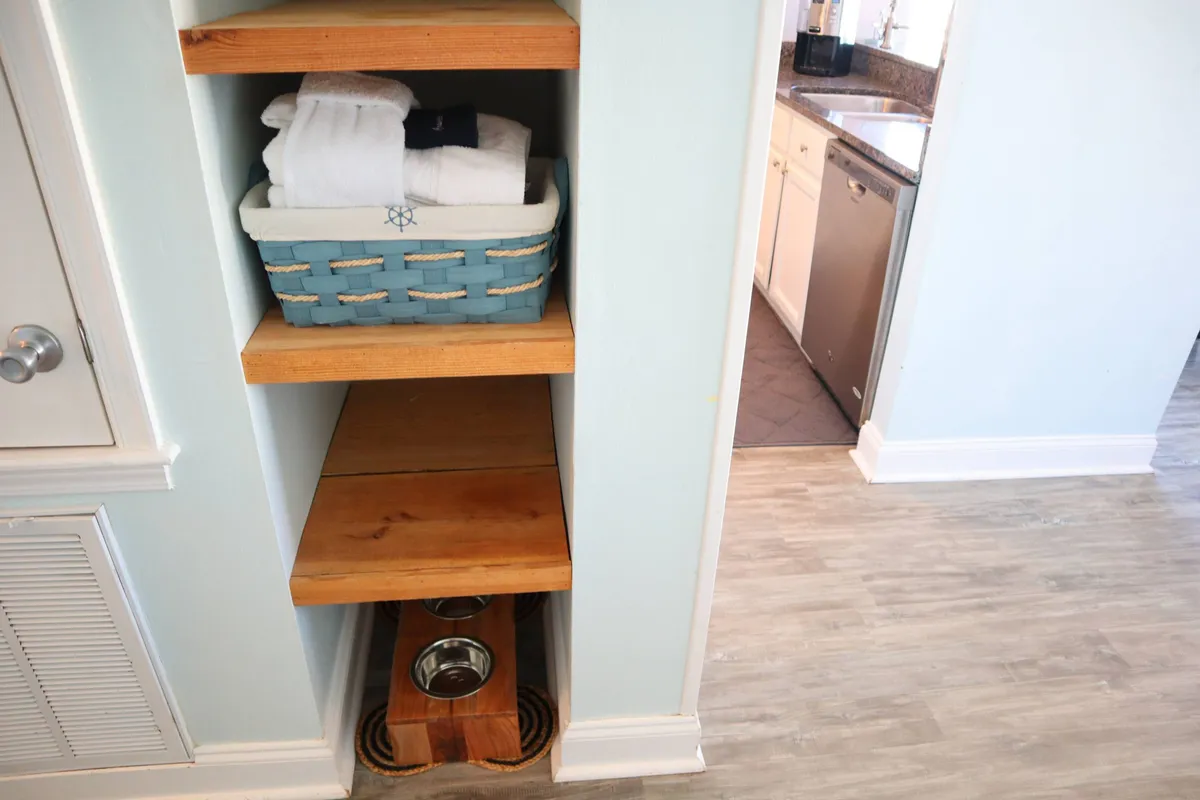 A close-up of a blue basket filled with towels, set atop wooden shelves, with a dedicated pet feeding station visible. The scene is cozy and practical, emphasizing the property's thoughtful pet-friendly touches and amenities.