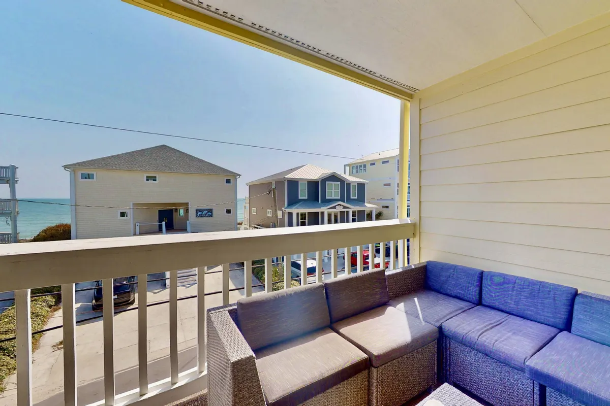 A cozy outdoor seating area on a private deck, offering a clear ocean view and surrounded by neighboring beach houses. The setting invites relaxation, with ample space to lounge and unwind after beach outings.